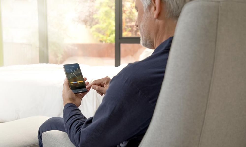 Man adjusting home settings using a mobile app while seated in a bright room