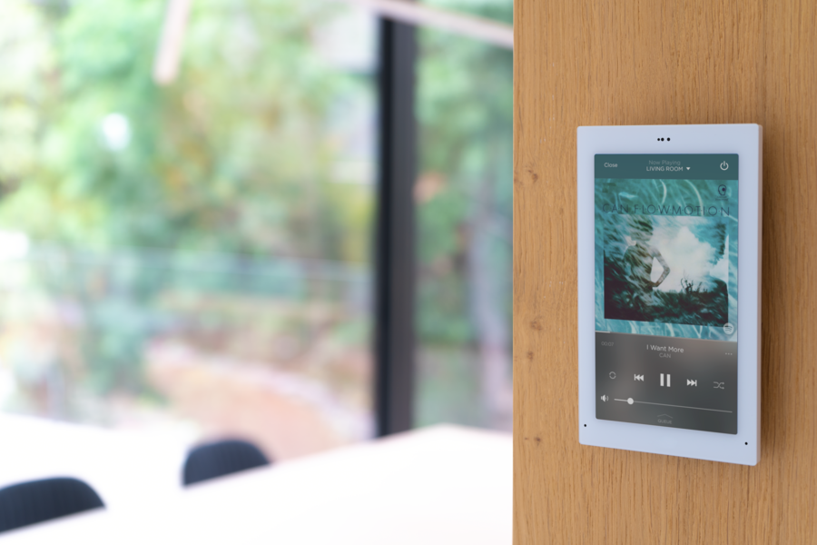 A wall-mounted Savant touch panel displaying the song currently playing.