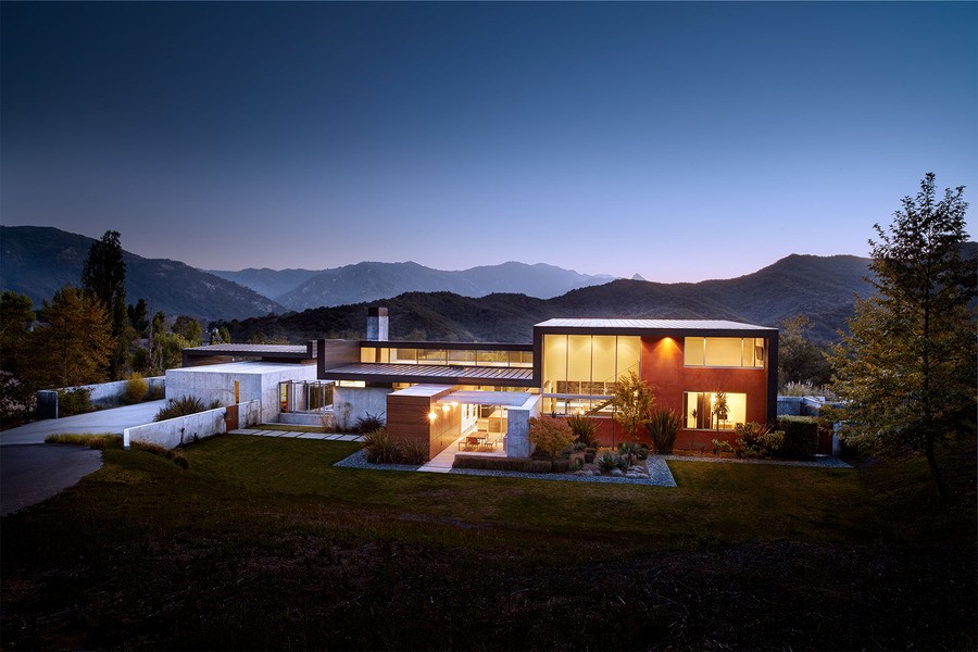 A modern house in the evening with mountains in the background, glowing from the luxury lights inside.