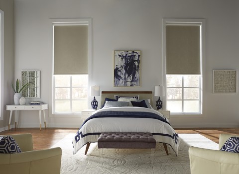 A bedroom featuring minimalist decor and plush textures, complemented by understated window shades that invite natural light in. 