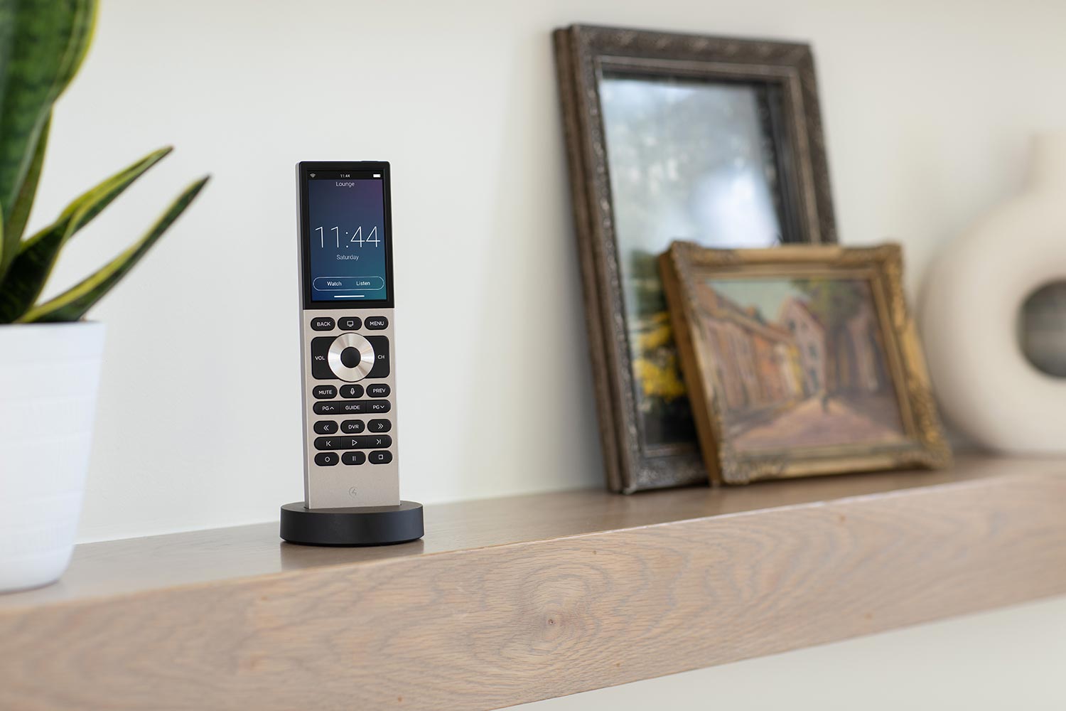 Smart remote control on a wooden shelf next to framed artwork