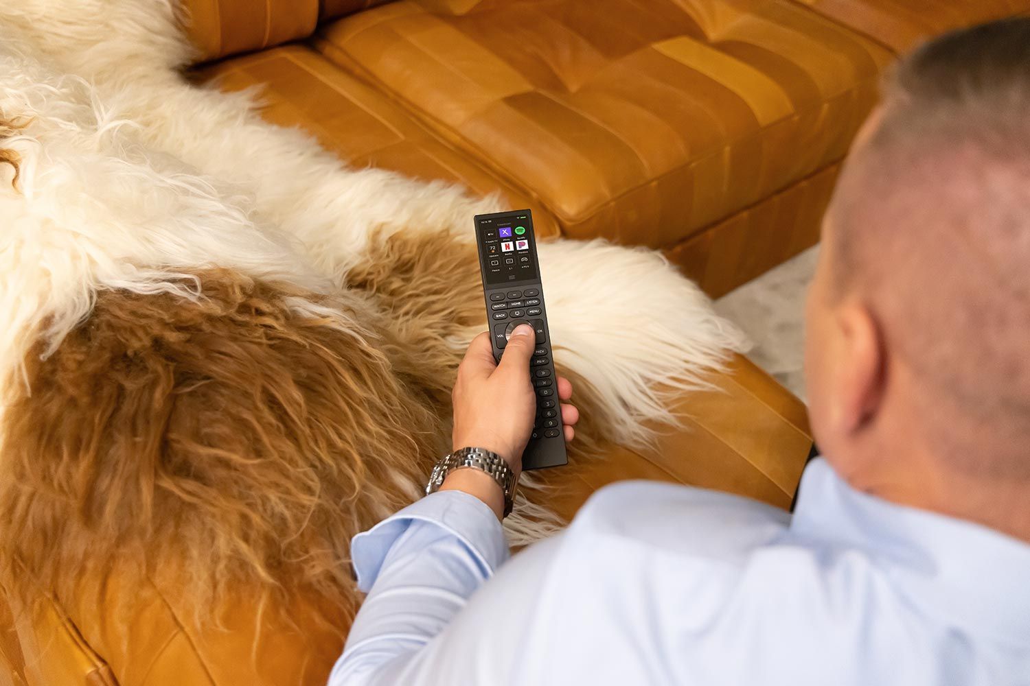 Person using a smart remote control while seated on a leather sofa